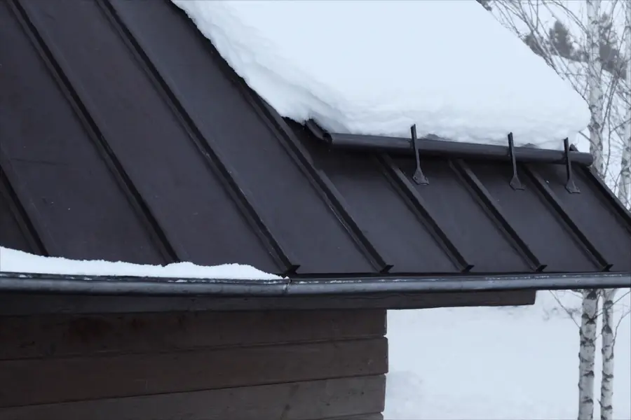 Snow retention bar holding settled snowpack above the eave of a standing seam metal roof in the North Country, New York